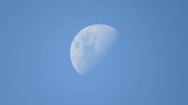 A half-lit moon in a daytime blue sky